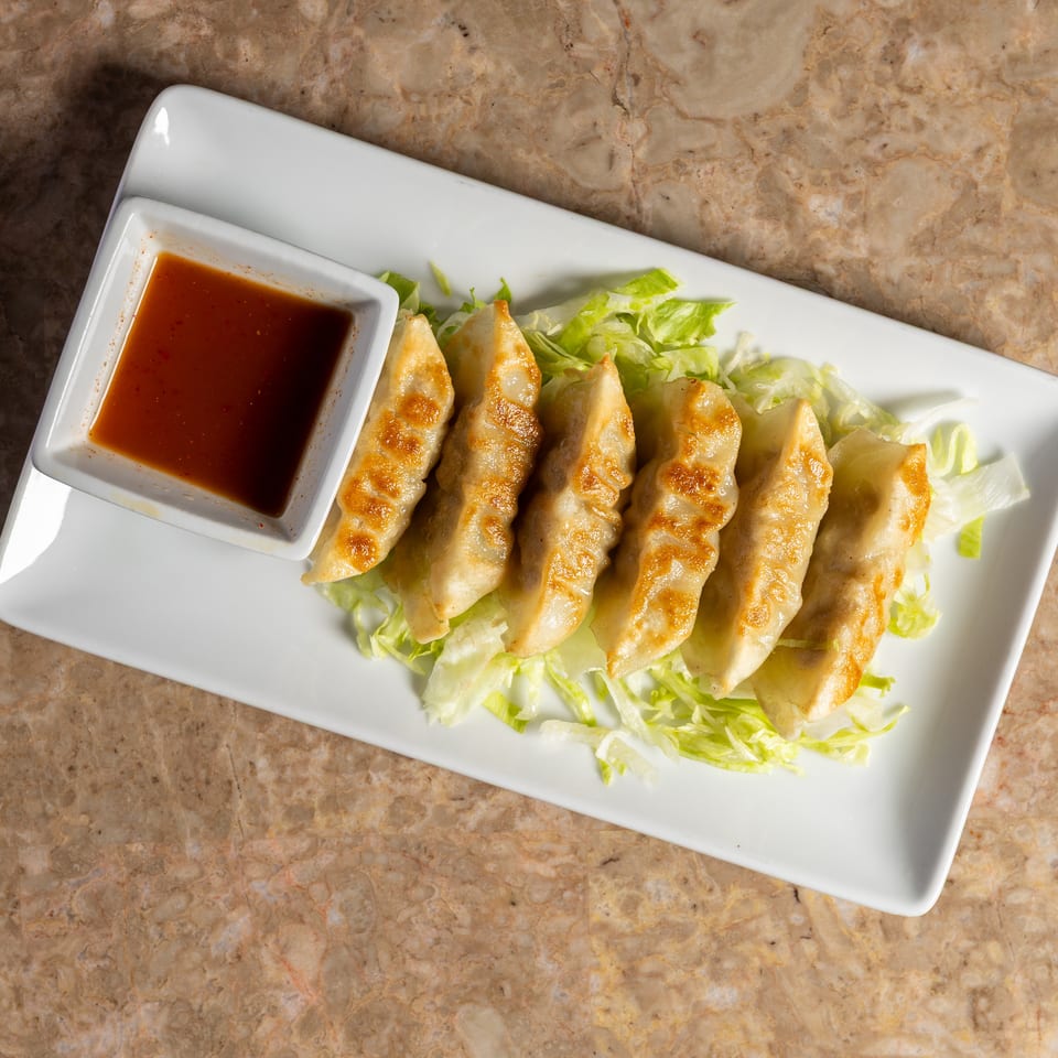 Six pan-fried dumplings with a side of dipping sauce on a bed of shredded lettuce.