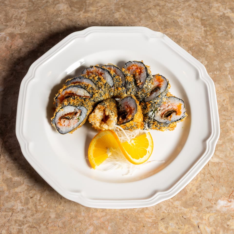 Fried sushi rolls with orange slices and shredded garnish on a white plate.