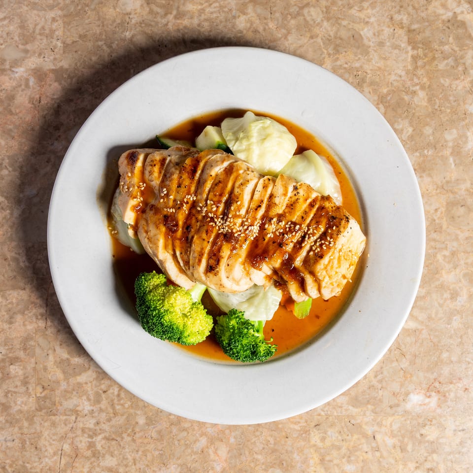 Grilled chicken breast, sliced and drizzled with sauce, served with broccoli and cabbage.