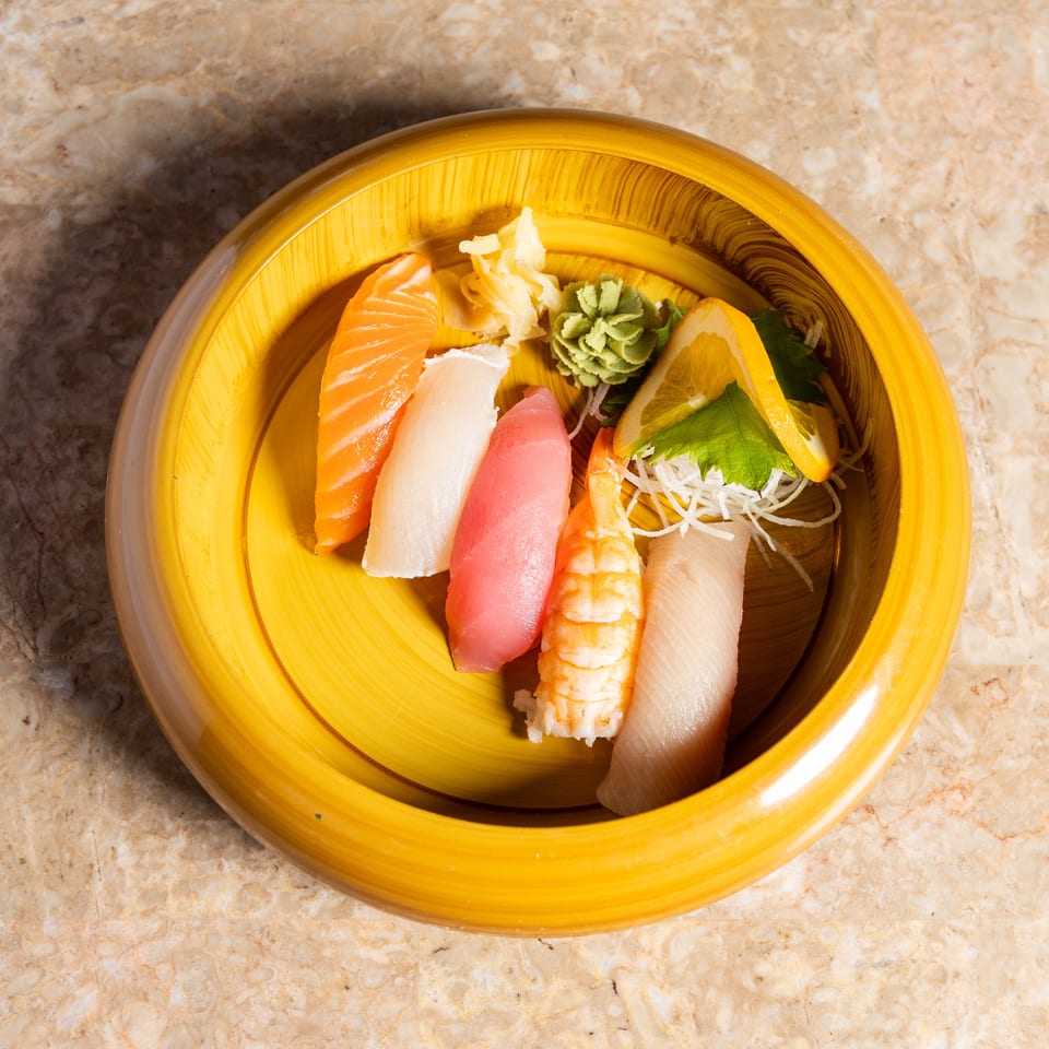 Assorted nigiri sushi with salmon, tuna, shrimp, and white fish, served in a yellow bowl.