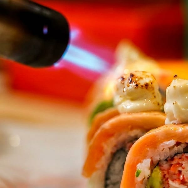 Blowtorch searing creamy topping on salmon and avocado sushi rolls.