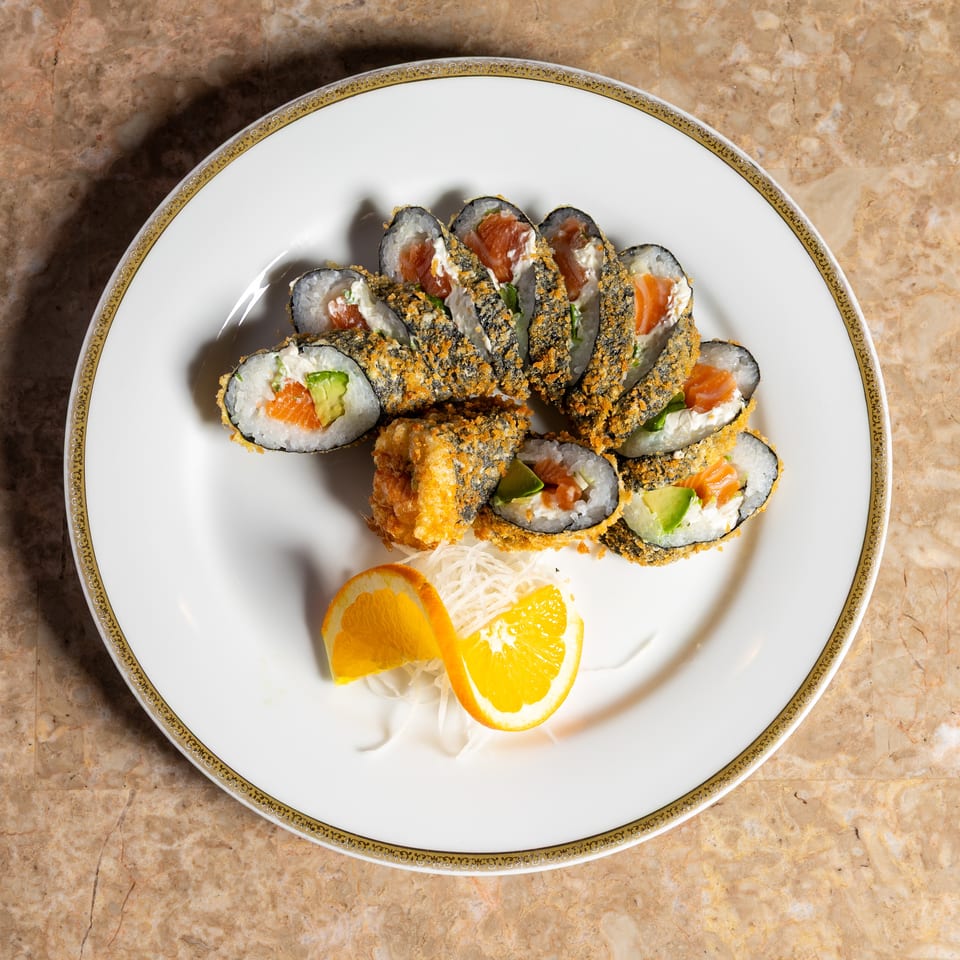Crispy fried sushi rolls with salmon, cream cheese, and avocado, garnished with orange slices.