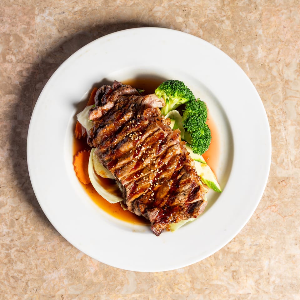 Grilled steak with sesame seeds, broccoli, carrots, and cabbage on a white plate.