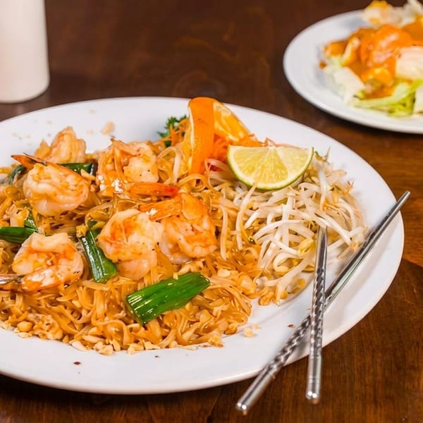 Plate of shrimp Pad Thai with lime, bean sprouts, and chopsticks, with a side salad.