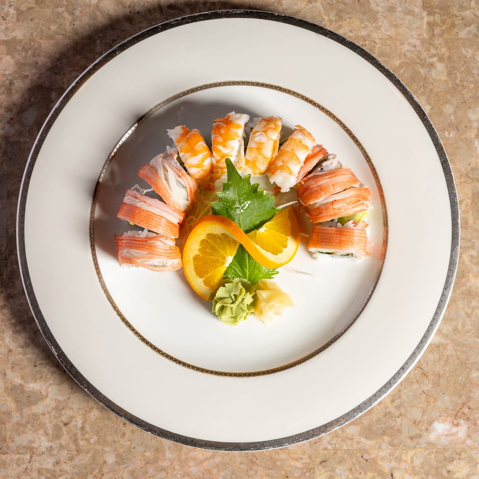 Sushi rolls with shrimp and crab, garnished with orange slices, wasabi, and ginger on a white plate.