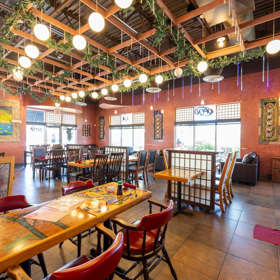 A restaurant dining room with red walls, wooden tables, red chairs, and festive ceiling decorations.