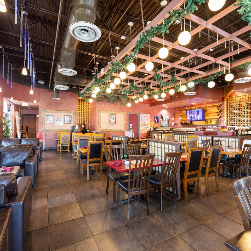 Spacious restaurant interior with various seating, including booths, tables, and a sushi bar, under decorative lighting.