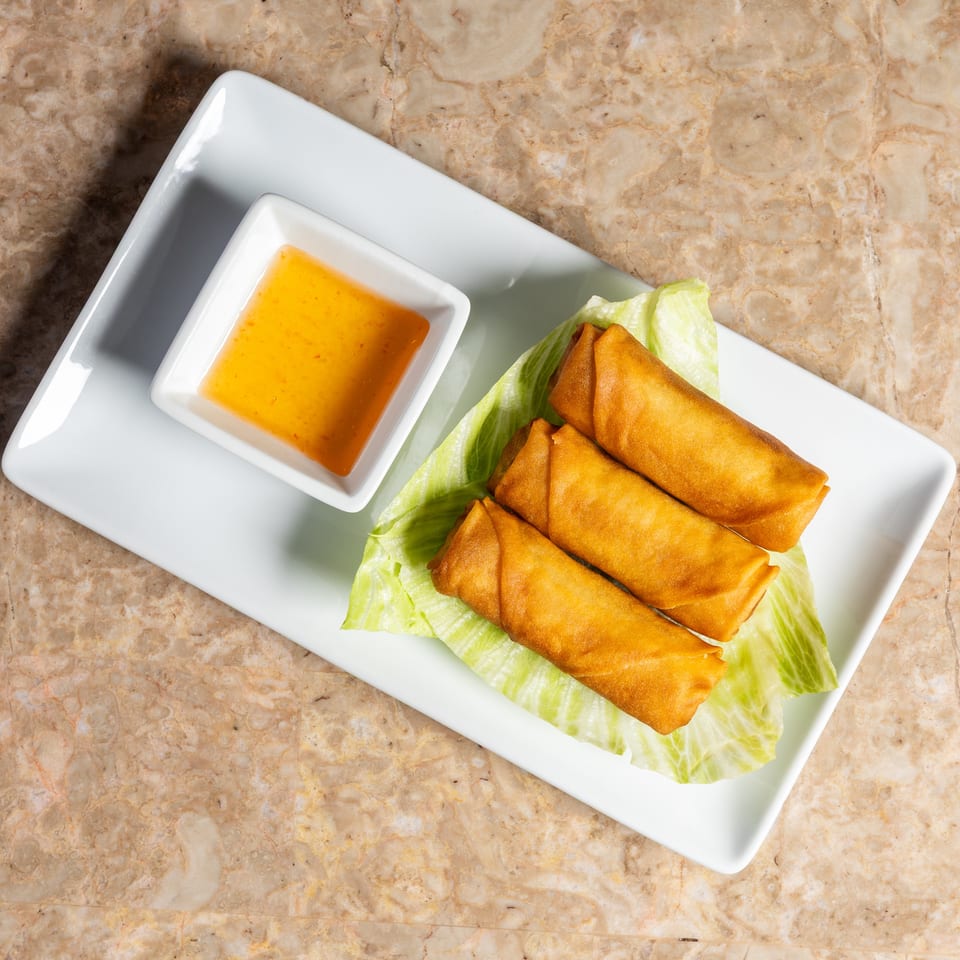 Three crispy golden spring rolls on lettuce with a side of orange dipping sauce.