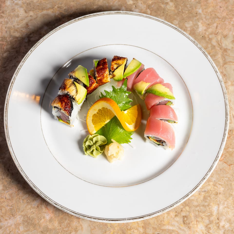 Sushi roll with eel and avocado on one side, tuna and avocado on the other, garnished with orange slices.